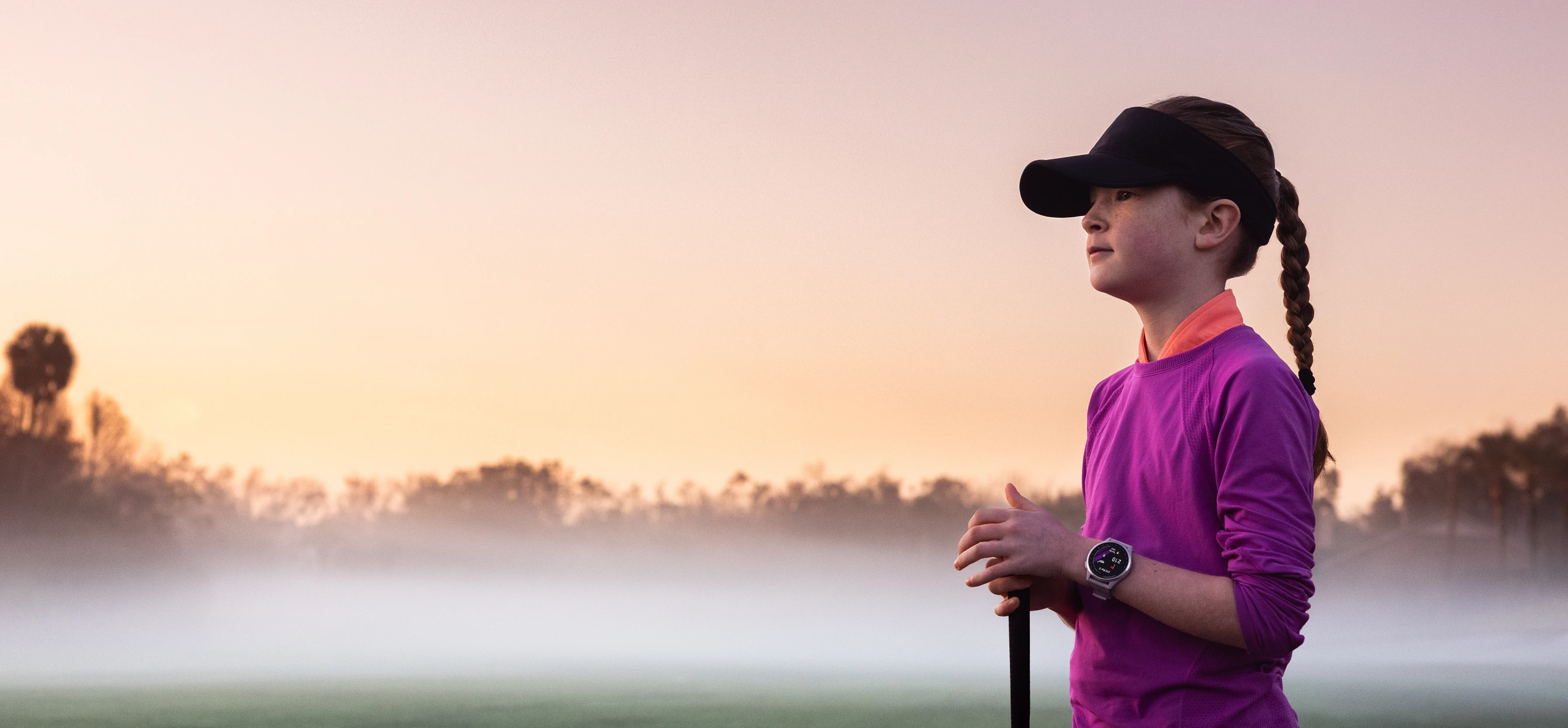 Zdjęcie dziewczyny idącej po polu golfowym z zegarkiem Appoach J1 na ręku i kijem golfowym patrząca w dal